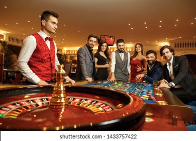 Group happy friends make bets gambiling at the roulette table in the casino.