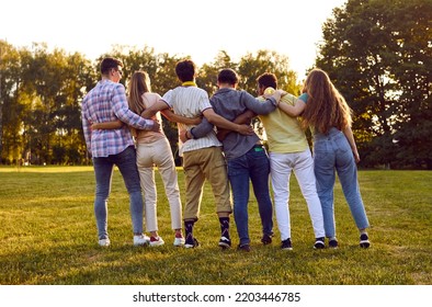 Group of happy friends meet on a nice summer day. Backside shot of several young men and women huddling in park. Back view of diverse people standing in row on green grass lawn and hugging each other - Powered by Shutterstock