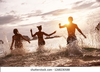 Group Of Happy Friends Run And Jump At Sunset Sea Beach. Tropical Vacations Concept