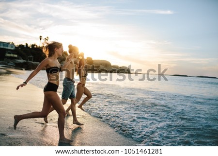 Group of happy friends running to the sea on sunset. Joyful friends having fun on summer vacation at beach.