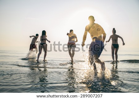 Group of happy friends running in to water at sunset - Silhouettes of active people having fun on the beach on vacation - Tourists going to swim on a tropical island