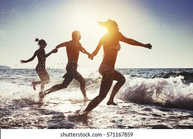 Group of happy friends runs to the sea. Tropical beach at sunny evening