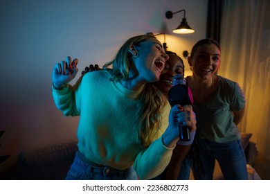 Group of happy friends singing karaoke during a girls night party at the apartment, singing and dancing. - Powered by Shutterstock
