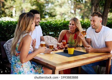 Group Of Happy Friends Sitting At A Table In A Summer Bar Smiling And Drinking Beer