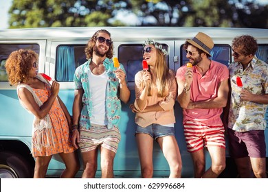 Group of happy friends standing with ice lolly in front of camper van in park