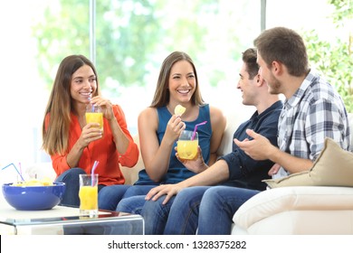 Group Of Happy Friends Talking Eating Chips And Drinking Refreshments Sitting On A Couch In The Living Room At Home