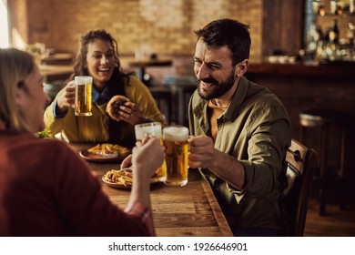 Group of happy friends toasting with beer while having lunch in a pub. Focus is on man. 
