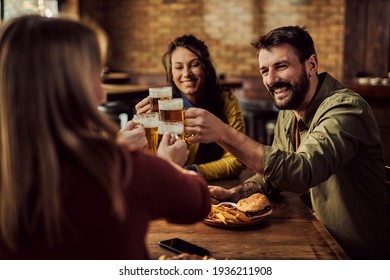 Group of happy friends toasting with beer while gathering in a bar. Focus is on man. 