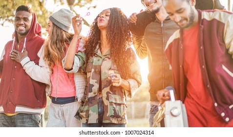 Group of happy friends walking and listening music in city park - Friendship and diverse cultures concept with trendy young people having fun together - Focus on two left guys faces