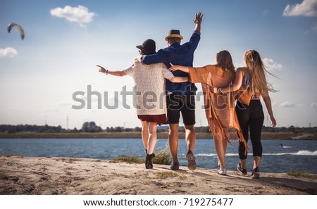 Group of happy friends walking on beach, fashion styled
