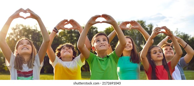 Group of happy good kind little children standing in row in green sunny summer park, looking at peaceful skies up above, raising hands, and doing heart gestures. Banner, header. Love and peace concept - Powered by Shutterstock