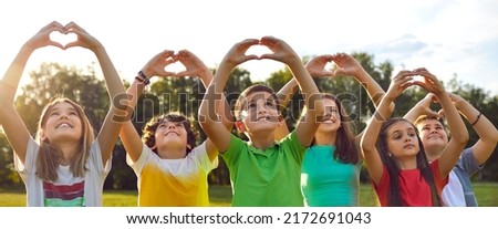 Group of happy good kind little children standing in row in green sunny summer park, looking at peaceful skies up above, raising hands, and doing heart gestures. Banner, header. Love and peace concept
