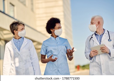 Group Of Happy Healthcare Workers Wearing Face Masks While Walking Outdoor And Talking During Coronavirus Epidemic. 