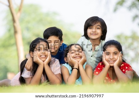 Group of happy Indian children lying on green grass outdoors in spring park, Playful asian kids in the garden.