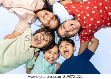 Group of happy Indian kids in circle looking down and embracing playing outdoor, Playful asian children together, looking at camera. Summer season background. 