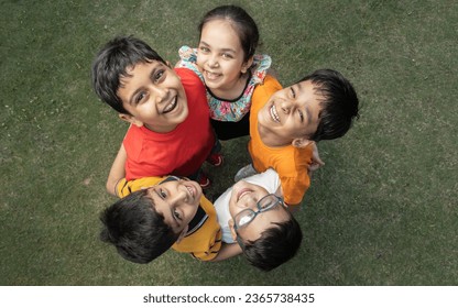 Group of happy Indian kids standing in circle together looking up at the camera in the summer park, Playful asian children together at outdoor garden. View from above. Background.