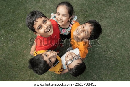 Group of happy Indian kids standing in circle together looking up at the camera in the summer park, Playful asian children together at outdoor garden. View from above. Background.