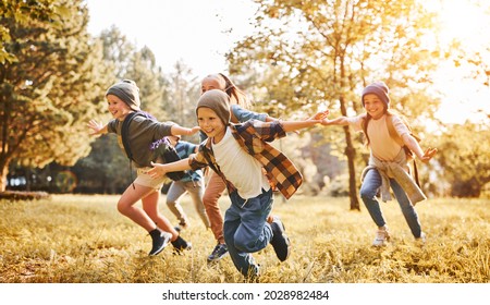 Group of happy joyful school kids with backpacks running with outstretched arms in forest on sunny spring day, excited children scouts boys and girls having fun during camping activity in nature - Shutterstock ID 2028982484
