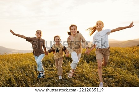 Group of happy joyful school kids   running and holding hands in field on sunny spring day, excited children   boys and girls enjoying summer holidays in countryside