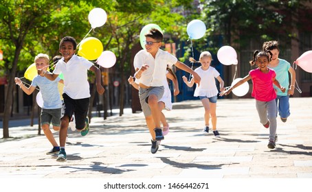 Group Of Happy Kids With Balloons Running In Race In The Street And Laughing Outdoors 