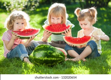 Group Of Happy Kids Eating Watermelon On Green Grass In Summer Park