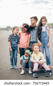 Group Of Happy Kids Outdoors. Redhead Girl And African Girlsitting On Skateboard. The Concept Of Friendship And Intercultural Communication