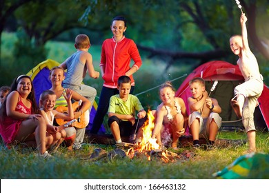 Group Of Happy Kids Roasting Marshmallows On Camp Fire
