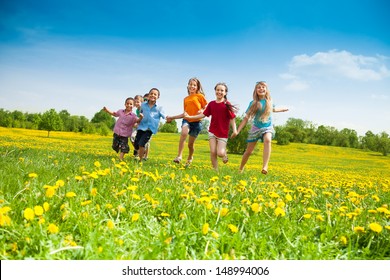 Group of happy kids running in the yellow flowers field summer day