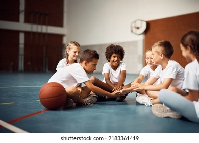 Group Of Happy Kids Sitting In Circle And Joining Hands In Unity While Having Physical Activity Class At School Gym. Focus Is On African American Boy.