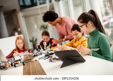 Group of happy kids with their African American female science teacher with laptop programming electric toys and robots at robotics classroom - Powered by Shutterstock