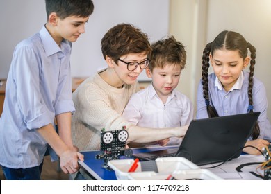 group of happy kids with their female adult science prof with tablet pc computer programming electric toys and robots at robotics hobby club