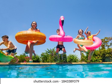 Group Of Happy Little Kids Dive In Water With Inflatable Toys Flamingo Doughnut Jump Into The Swimming Pool