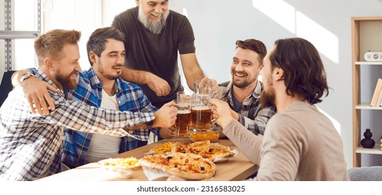 Group of happy men enjoying free time, having a party at home, sitting at a table, drinking beer, clinking mugs, eating pizza, and having fun together. Banner background. Friends' party concept - Powered by Shutterstock