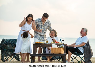 Group of Happy multi generation Asian family enjoy dinner party together on the beach at sunset. Parents with senior grandparents and cute child girl relax and having fun on summer holiday vacation - Powered by Shutterstock