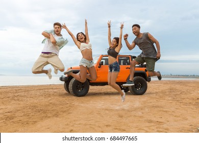 Group Of Happy Multiethnic Friends Jumping In Front Of Their Car With Hands Raised And Having Fun At The Beach