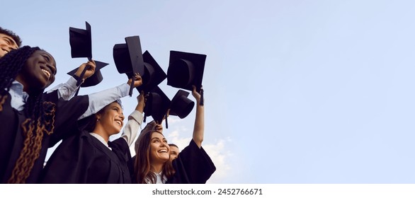 Group of happy multiethnic high school, college or university students having fun on graduation day and raising their graduate hats up to clear blue sky. Copy space banner background - Powered by Shutterstock