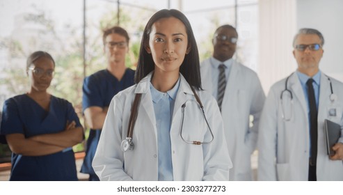 Group of Happy Multiethnic Team of Female and Male Doctors, Nurses and Healthcare Professionals Posing for Camera and Smiling. Portrait of a Confident Asian Physician Standing First in Focus - Powered by Shutterstock