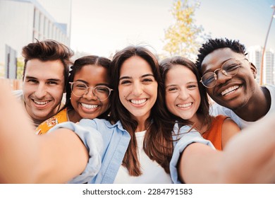Group of happy multiracial teenagers having fun smiling taking a selfie portrait together on a students meeting. Five multiethnic young friends laughing and taking a photo with a smartphone. High