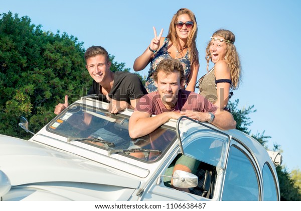 Group of happy people in a car at sunset in\
summer, ready for a\
roadtrip.