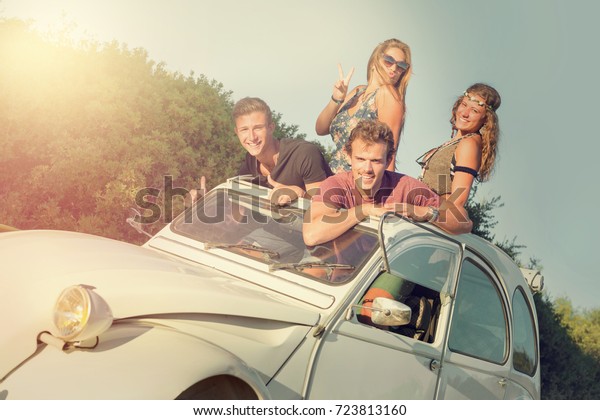 Group of happy people in a car at sunset in\
summer, ready for a\
roadtrip.