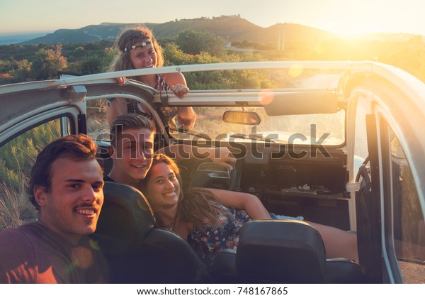 Group of
happy people in a car at sunset in
summer.