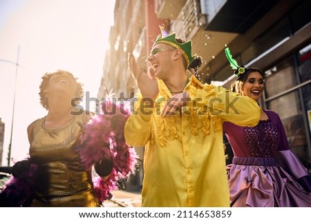 Group of happy people in carnival costumes dancing and having fun during Mardi Gras festival on the street. 