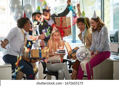 Group of happy people celebrating colleague's birthday with confetti and cake