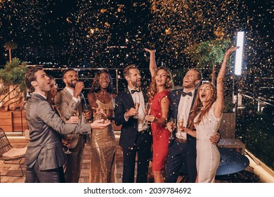 Group of happy people in formalwear having fun together with confetti flying all around - Powered by Shutterstock