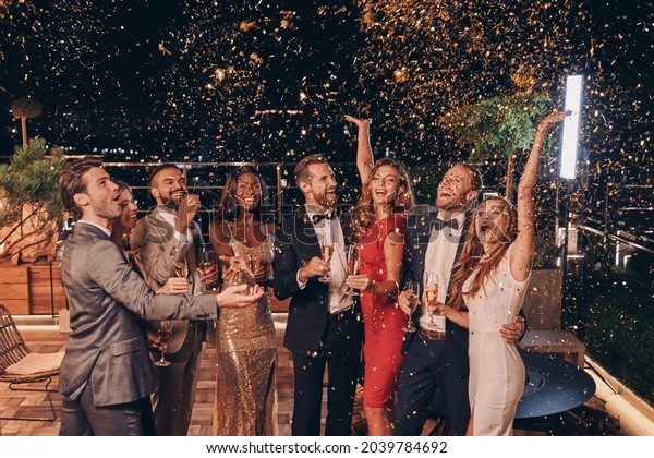 Group of happy people in formalwear\
having fun together with confetti flying all\
around