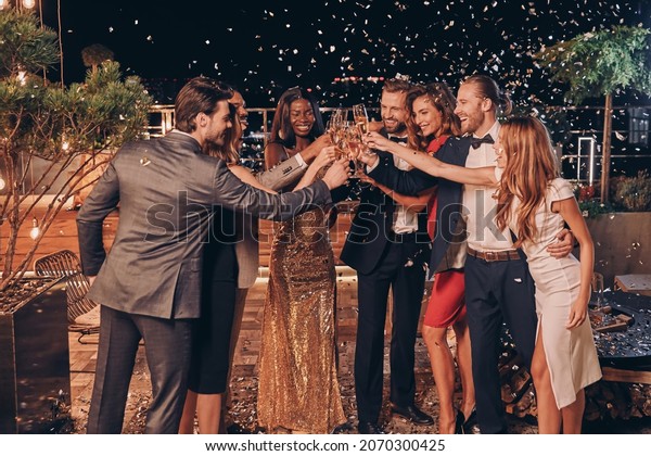 Group of happy people in formalwear\
toasting with champagne with confetti flying all\
around