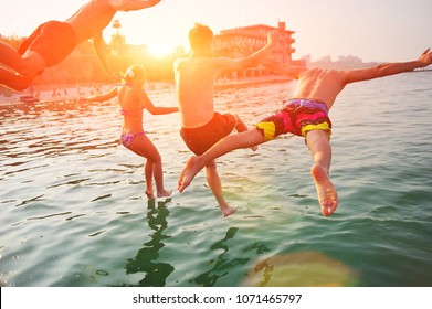 Group of happy people having fun jumping in summer sea water from a beach pier. Friends team in mid air on a sunny day summer pool beach party. Summer vacation, youth friendship, beach cruise concept.