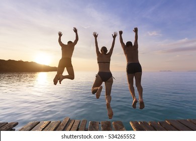 Group Of Happy People Having Fun Jumping In The Sea Water From A Pier