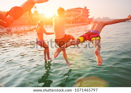 Group of happy people having fun jumping in summer sea water from a beach pier. Friends team in mid air on a sunny day summer pool beach party. Summer vacation, youth friendship, beach cruise concept.