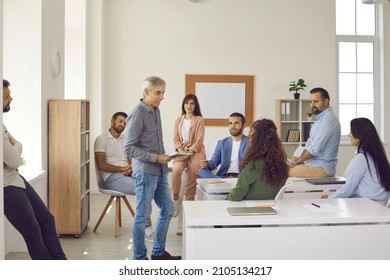 Group Of Happy People Meeting For Training Session With Mentor. Team Of Adult Students Or Company Workers Sitting At Desks In Classroom Or Modern Office Listening To Experienced Senior Business Coach